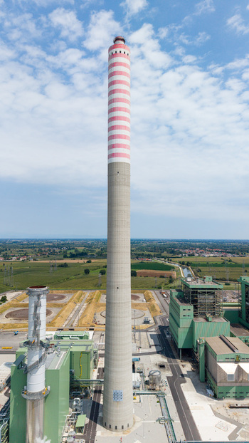 Aerial view of a modern combined cycle natural gas power station with a tall striped chimney stack industrial buildings and green fields in Tavazzano con Villavesco Lombardy Italy.