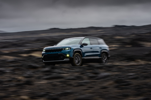 View of a blue SUV driving across a dark volcanic landscape in Reykjavik Reykjavikurborg Iceland.