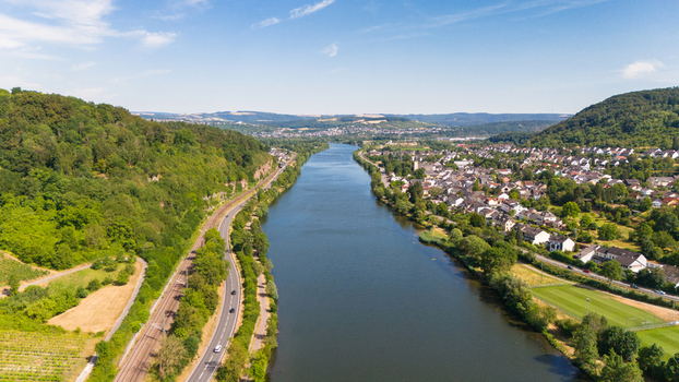 Aerial view of the Moselle River flowing through a scenic valley with a village railway tracks and lush green hills in Trier Saarburg Rhineland Palatinate Germany.