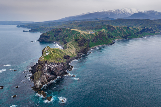 Aerial view of Cape Kamui with its lighthouse perched on rocky cliffs surrounded by the sea and distant snow capped mountains in Otaru Hokkaido Japan. Aerial view of Cape Kamui with its lighthouse perched on rocky cliffs surrounded by the sea and distant snow capped mountains in Otaru Hokkaido Japan.