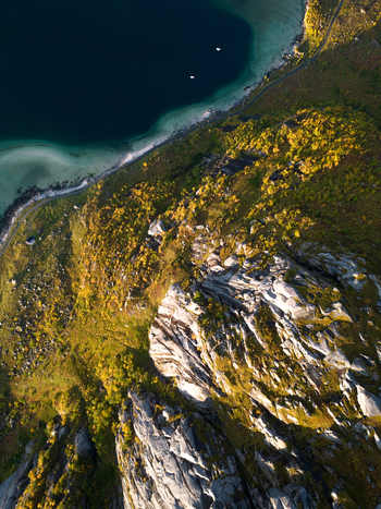 Aerial view of the rugged granite peaks of Tangstad with golden autumn foliage and dark blue sea in Leknes Nordland Norway. Aerial view of the rugged granite peaks of Tangstad with golden autumn foliage and dark blue sea in Leknes Nordland Norway.