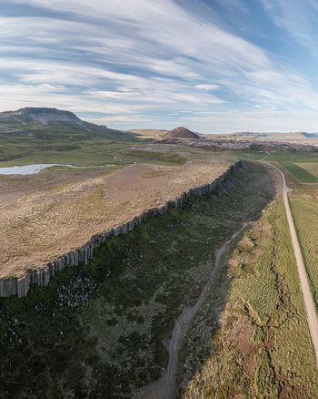 Aerial view of the basalt columns of Gerduberg Cliffs surrounded by green fields volcanic terrain and a dirt road in Raudhamelur Eyja og Miklaholtshr Iceland. Aerial view of the basalt columns of Gerduberg Cliffs surrounded by green fields volcanic terrain and a dirt road in Raudhamelur Eyja og Miklaholtshr Iceland.
