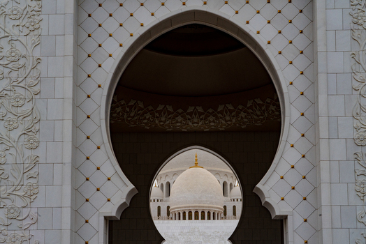 View of an ornate white marble archway with floral carvings framing a large dome of a grand mosque in Abu Dhabi Abu Dhabi United Arab Emirates. View of an ornate white marble archway with floral carvings framing a large dome of a grand mosque in Abu Dhabi Abu Dhabi United Arab Emirates.
