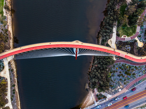 Aerial view of Boorloo Bridge with its distinctive red pedestrian path spanning the Swan River surrounded by lush parkland and urban roads in East Perth Western Australia Australia.