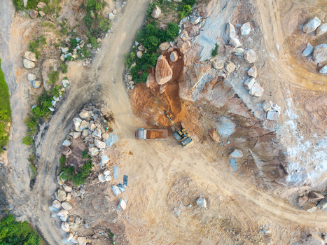 Aerial view of a mining site with an excavator loading a dump truck amidst rocky terrain and dirt paths in Bukit Tambun Penang Malaysia. Aerial view of a mining site with an excavator loading a dump truck amidst rocky terrain and dirt paths in Bukit Tambun Penang Malaysia.