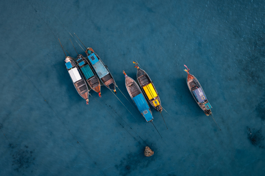 Aerial view of traditional Thai long tail boats floating on the clear blue water of Pi Leh Bay in Tambon Ao Nang Chang Wat Krabi Thailand. Aerial view of traditional Thai long tail boats floating on the clear blue water of Pi Leh Bay in Tambon Ao Nang Chang Wat Krabi Thailand.