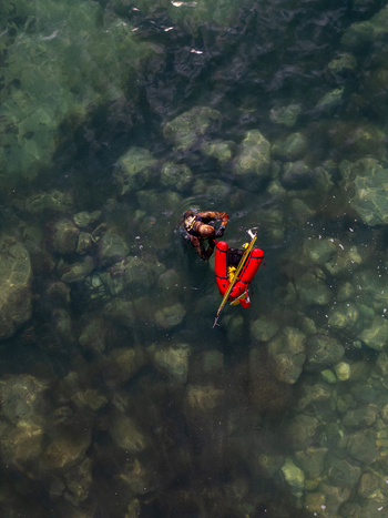 Aerial view of a diver with a red safety float swimming in the clear rocky waters of Cala Llebeig in El Poble Nou de Benitatxell Valencian Community Spain.