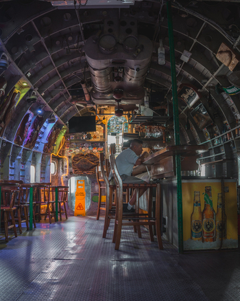 View of the interior of an airplane fuselage converted into a bar with a man sitting at the counter metal structural ribs and a yellow caution sign in Costa Rica.