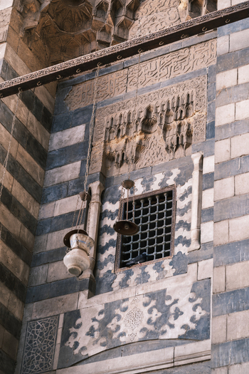 View of the intricate stone carvings and hanging lamps on the facade of the Al Ghuri Dome in Cairo Egypt. View of the intricate stone carvings and hanging lamps on the facade of the Al Ghuri Dome in Cairo Egypt.