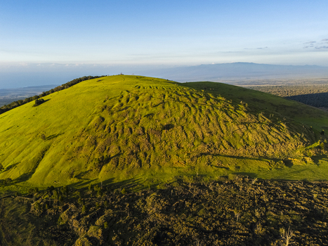 Aerial view of the Puu Waawaa cinder cone featuring vibrant green slopes and volcanic ridges above dark lava fields in Hawaii County Hawaii United States. Aerial view of the Puu Waawaa cinder cone featuring vibrant green slopes and volcanic ridges above dark lava fields in Hawaii County Hawaii United States.