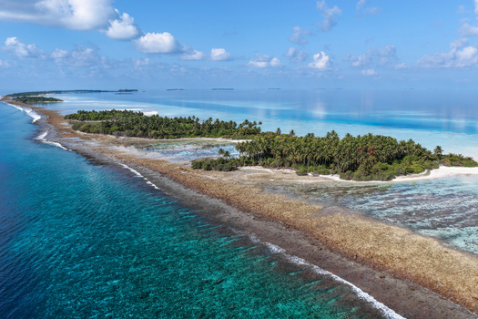 Aerial view of lush tropical islands with green palm trees and turquoise coral reefs surrounded by the deep blue ocean under a clear sky near Vaanee Dhaalu Atoll Maldives. Aerial view of lush tropical islands with green palm trees and turquoise coral reefs surrounded by the deep blue ocean under a clear sky near Vaanee Dhaalu Atoll Maldives.