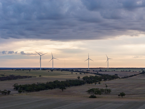 Aerial view of wind turbines standing in a vast rural landscape with rolling fields scattered trees and a dramatic cloudy sky at sunset in Kiata Victoria Australia. Aerial view of wind turbines standing in a vast rural landscape with rolling fields scattered trees and a dramatic cloudy sky at sunset in Kiata Victoria Australia.