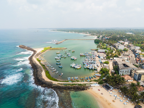 Aerial view of colorful fishing boats moored in the harbor protected by a stone breakwater along the sandy coastline in Hikkaduwa Southern Province Sri Lanka. Aerial view of colorful fishing boats moored in the harbor protected by a stone breakwater along the sandy coastline in Hikkaduwa Southern Province Sri Lanka.