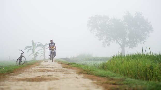 View of a man riding a bicycle on a foggy rural path Bangladesh. View of a man riding a bicycle on a foggy rural path Bangladesh.
