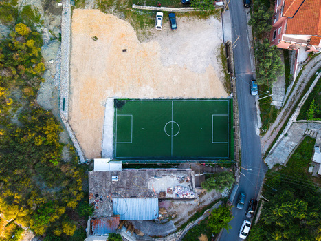 Aerial view of a small green artificial turf football pitch surrounded by a gravel lot and residential buildings in Kruje Durres County Albania.