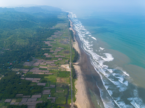 Aerial view of the long sandy beach with waves crashing on the shore a coastal road and lush green hills in Cox s Bazar Chittagong Division Bangladesh. Aerial view of the long sandy beach with waves crashing on the shore a coastal road and lush green hills in Cox s Bazar Chittagong Division Bangladesh.