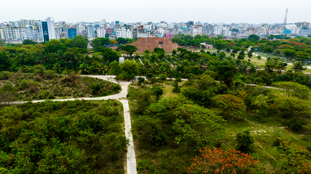 Aerial view of the Rayer Bazaar Memorial surrounded by lush greenery walking paths and the urban skyline of Dhaka Dhaka Division Bangladesh.