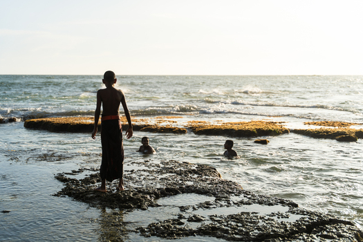 Sri Lanka 11 January 2026 View of children playing in the shallow ocean waters near a rocky reef during golden hour.