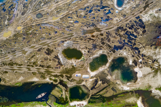 Aerial view of the rugged landscape featuring scattered water pools dirt tracks and a small boat moored in a river channel in Panchagarh Rangpur Division Bangladesh. Aerial view of the rugged landscape featuring scattered water pools dirt tracks and a small boat moored in a river channel in Panchagarh Rangpur Division Bangladesh.