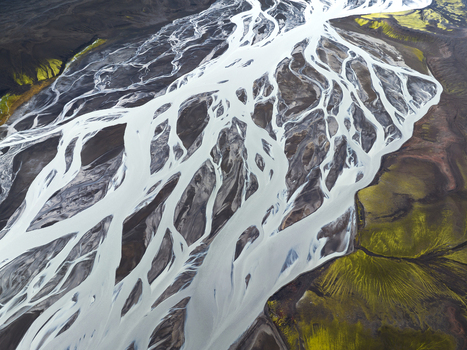 Aerial view of glacial rivers carving through volcanic sands and mossy terrain creates a mesmerizing contrast of white black and green Highlands Iceland.