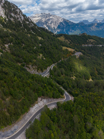Aerial view of a winding mountain road through the lush green forests of the Albanian Alps under a cloudy sky in Shkoder Shkoder County Albania. Aerial view of a winding mountain road through the lush green forests of the Albanian Alps under a cloudy sky in Shkoder Shkoder County Albania.