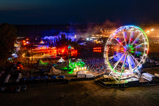 Herzogenaurach Germany 22 July 2022 Aerial view of the Open Beatz Festival featuring a large illuminated Ferris wheel bright stage lights and crowds of people at night. Herzogenaurach Germany 22 July 2022 Aerial view of the Open Beatz Festival featuring a large illuminated Ferris wheel bright stage lights and crowds of people at night.