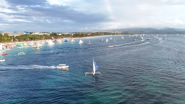 Malay Philippines 02 May 2026 Aerial view of Boracay Island with numerous sailboats on the turquoise water along the white sand beach under a cloudy sky with a faint rainbow.