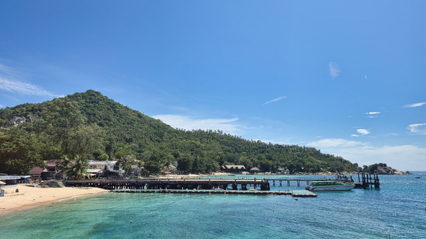 Ko Tao Surat Thani Thailand 23 September 2025 View of Ko Tao featuring a wooden pier extending into turquoise water with a lush green mountain in the background under a blue sky.