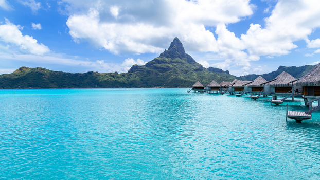 View of overwater bungalows over a turquoise lagoon with Mount Otemanu in the background in Bora Bora Leeward Islands French Polynesia.