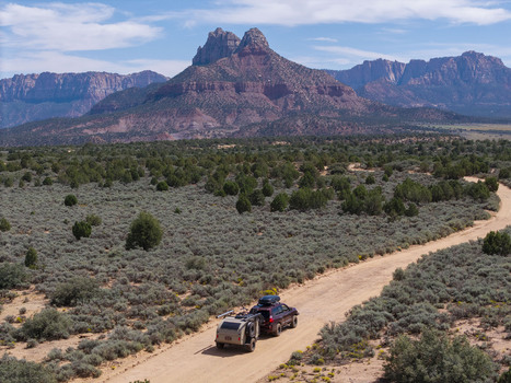 Aerial view of an SUV pulling a teardrop camper trailer on a dirt road on Gooseberry Mesa with the red rock landscape of Zion National Park in the background Hurricane Utah United States. Aerial view of an SUV pulling a teardrop camper trailer on a dirt road on Gooseberry Mesa with the red rock landscape of Zion National Park in the background Hurricane Utah United States.