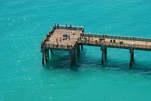 Aerial view of Juno Beach Pier with people fishing on the wooden deck over turquoise ocean waters in Juno Beach Florida United States. Aerial view of Juno Beach Pier with people fishing on the wooden deck over turquoise ocean waters in Juno Beach Florida United States.