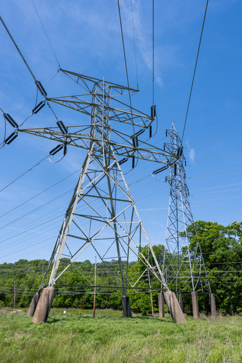 View of high voltage electricity pylons standing in a grassy field at Greentree Park under a clear blue sky in Kirkwood Missouri United States. View of high voltage electricity pylons standing in a grassy field at Greentree Park under a clear blue sky in Kirkwood Missouri United States.
