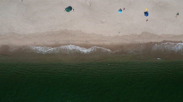 Aerial view of the sandy beach with colorful umbrellas and gentle waves washing onto the shore in Mantoloking New Jersey United States.