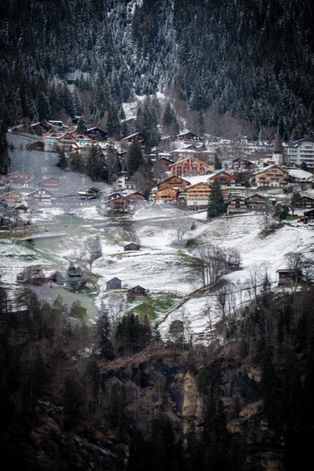 View of a charming village nestled amongst snow dusted fields and dark looming forests under a cloudy sky Lauterbrunnen Switzerland. View of a charming village nestled amongst snow dusted fields and dark looming forests under a cloudy sky Lauterbrunnen Switzerland.