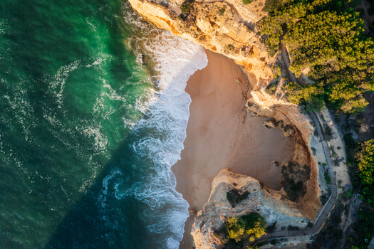 Aerial view of the golden cliffs and sandy beach at Caramujeira with turquoise waves crashing against the shore in Lagoa Faro Portugal. Aerial view of the golden cliffs and sandy beach at Caramujeira with turquoise waves crashing against the shore in Lagoa Faro Portugal.