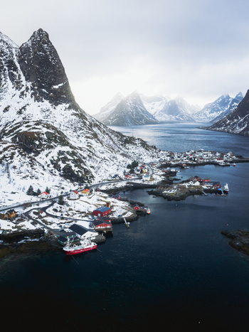 Aerial view of Reinebringen village nestled at the foot of snow dusted mountains reflecting in the deep blue fjord Reinebringen Nordland Norway.
