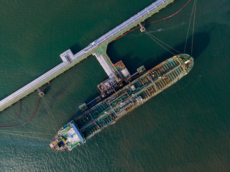 Aerial view of a large oil tanker docked at a fuel terminal pier with industrial piping and calm dark water in Cilacap Regency Central Java Indonesia. Aerial view of a large oil tanker docked at a fuel terminal pier with industrial piping and calm dark water in Cilacap Regency Central Java Indonesia.