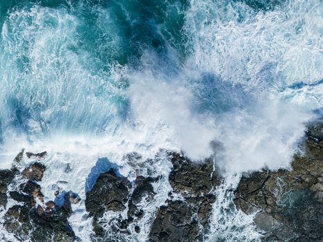 Aerial view of powerful turquoise waves crashing against the dark volcanic rocky shoreline of Kalaemamo with white sea foam Hawaii County Hawaii United States. Aerial view of powerful turquoise waves crashing against the dark volcanic rocky shoreline of Kalaemamo with white sea foam Hawaii County Hawaii United States.