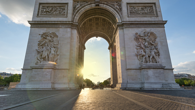 View of the Arc de Triomphe with intricate stone sculptures and the sun shining through the arch in Paris Ile de France France.