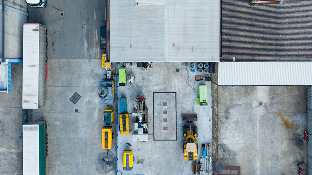 Aerial view of construction machinery including dump trucks and trailer mounted diesel generators parked on a concrete lot in an industrial area in Milan Lombardy Italy.