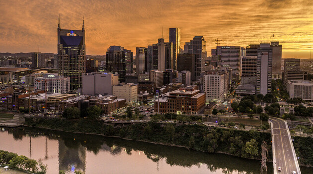 Aerial view of the downtown Nashville skyline at sunset featuring the Cumberland River modern skyscrapers and vibrant orange sky reflecting on the water in Nashville TN United States.