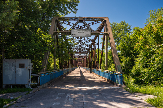View of the historic Old Chain of Rocks Bridge spanning the Mississippi River surrounded by lush green trees under a clear blue sky in St. Louis Missouri United States. View of the historic Old Chain of Rocks Bridge spanning the Mississippi River surrounded by lush green trees under a clear blue sky in St. Louis Missouri United States.