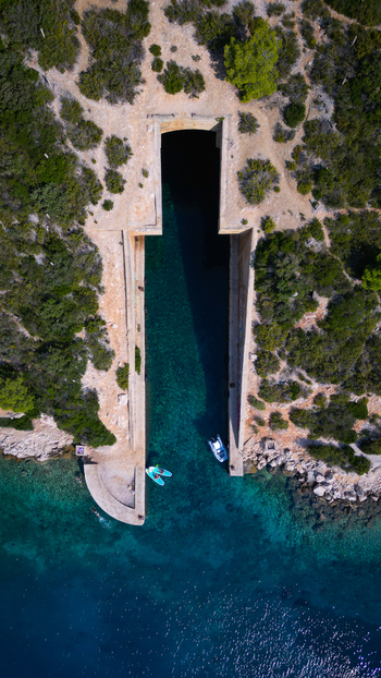 Aerial view of the Yugoslav army underground boat shelter Potkop Parja with turquoise water and paddleboarders at the entrance in Rogacic Splitsko dalmatinska Croatia. Aerial view of the Yugoslav army underground boat shelter Potkop Parja with turquoise water and paddleboarders at the entrance in Rogacic Splitsko dalmatinska Croatia.