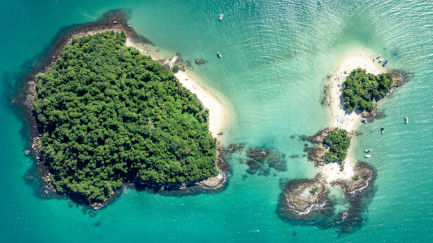 Aerial view of Ilha de Cataguas surrounded by turquoise waters lush green vegetation and small boats anchored near the sandy beaches in Angra dos Reis Rio de Janeiro Brazil.