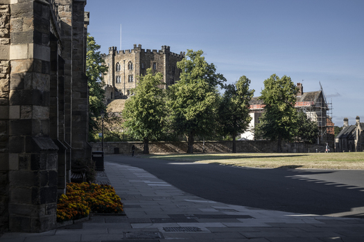 View of Durham Castle rising above the trees and stone walls with a paved walkway in the foreground and clear blue sky in Durham England United Kingdom. View of Durham Castle rising above the trees and stone walls with a paved walkway in the foreground and clear blue sky in Durham England United Kingdom.