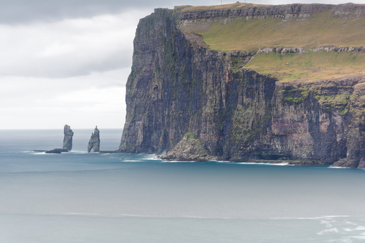 View of Risin og Kellingin sea stacks rising from the North Atlantic Ocean near the dramatic basalt cliffs of the Faroe Islands.
