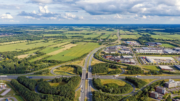 Aerial view of the cloverleaf interchange in Drachten surrounded by green fields industrial buildings and lush trees under a cloudy sky in Drachten Friesland Netherlands. Aerial view of the cloverleaf interchange in Drachten surrounded by green fields industrial buildings and lush trees under a cloudy sky in Drachten Friesland Netherlands.