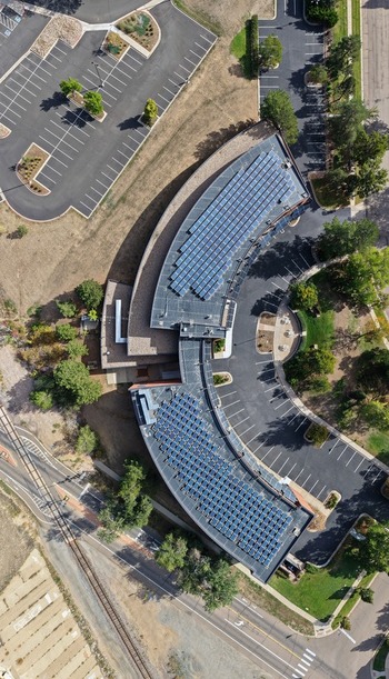 Aerial view of a modern building featuring extensive solar panel arrays on its curved roof surrounded by parking lots trees and nearby roads Boulder Colorado United States. Aerial view of a modern building featuring extensive solar panel arrays on its curved roof surrounded by parking lots trees and nearby roads Boulder Colorado United States.