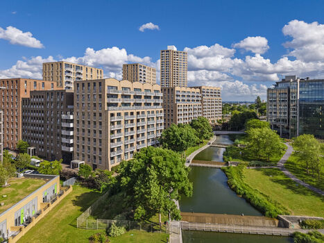 Aerial view of modern apartment buildings along a canal with green spaces and a blue sky in London England United Kingdom. Aerial view of modern apartment buildings along a canal with green spaces and a blue sky in London England United Kingdom.
