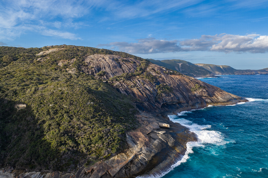 Aerial view of Salmon Holes featuring rugged granite cliffs lush coastal vegetation and turquoise ocean waves crashing against rocky shoreline in Torndirrup Western Australia Australia.